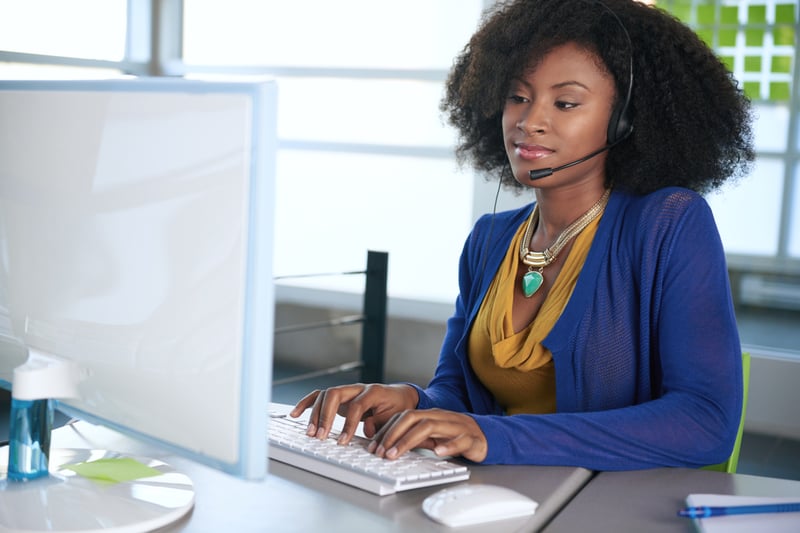 Portrait of a smiling customer service representative with an afro at the computer using headset-3